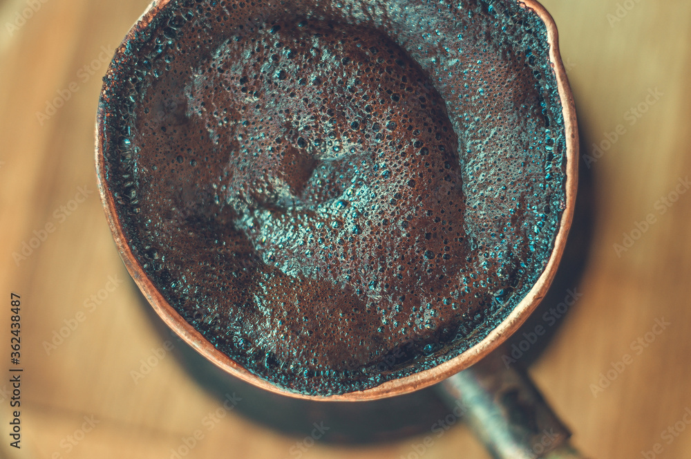Natural coffee with thick foam, brewed in a copper cezve in the classical way, on a wooden background, macro photo. Natural coffee with thick foam, brewed in a copper cezve in the classical way, on a wooden background, macro photo.