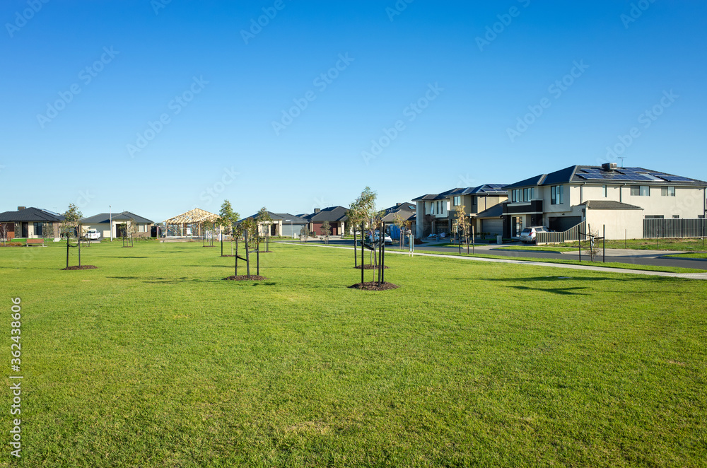 A public park with green lawn/grass and young trees surrounded by new residential houses/Australian homes in a Melbourne's suburb. Tarneit, VIC Australia. Background texture of a. suburban park. A public park with green lawn/grass and young trees surrounded by new residential houses/Australian homes in a Melbourne's suburb. Tarneit, VIC Australia. Background texture of a. suburban park.