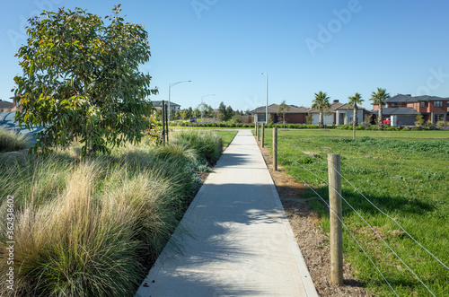 A pedestrian walkway/footpath leads to a residential neighbourhood with some modern Australian homes. Suburban view over a park with houses in the distance. Melbourne VIC Australia. photo