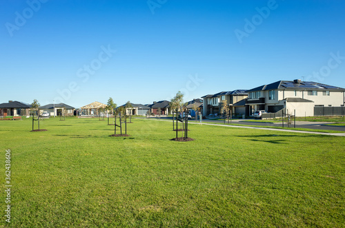 A public park with green lawn/grass and young trees surrounded by new residential houses/Australian homes in a Melbourne's suburb. Tarneit, VIC Australia. Background texture of a. suburban park.