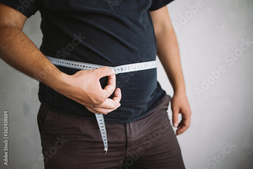 Overweight man measuring waist with measure tape, close up image. Weight loss, motivation, fat burning