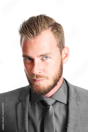 An attractive bearded male executive looking serious towards the camera wearing a black coat and tie.
