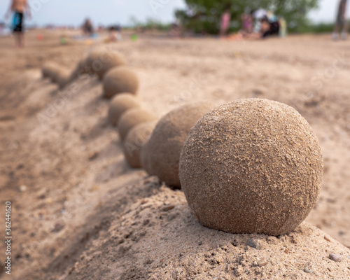 Close up view of an undulating sand castle hill or wall with perfectly smooth round balls or spheres of wet sand placed on serpentine shaped ridge as people crowd the beach beyond.