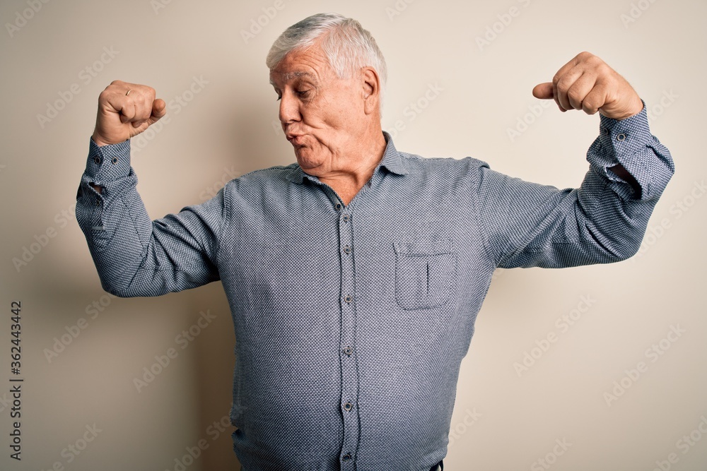 Senior handsome hoary man wearing casual shirt standing over isolated white background showing arms muscles smiling proud. Fitness concept. Senior handsome hoary man wearing casual shirt standing over isolated white background showing arms muscles smiling proud. Fitness concept.