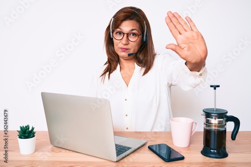 Fototapeta Middle age brunette hispanic woman working at the office wearing operator headse