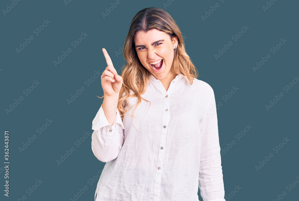 Young caucasian woman wearing casual clothes pointing finger up with successful idea. exited and happy. number one. Young caucasian woman wearing casual clothes pointing finger up with successful idea. exited and happy. number one.