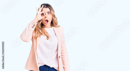 Young caucasian woman wearing business clothes doing ok gesture shocked with surprised face, eye looking through fingers. unbelieving expression.