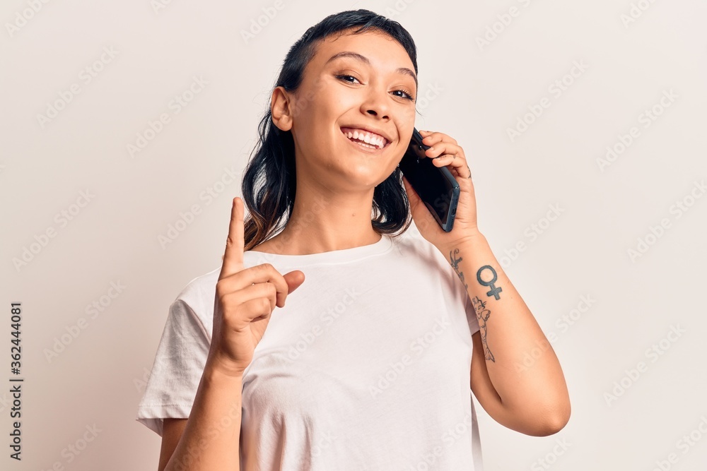 Young woman having conversation talking on the smartphone smiling with an idea or question pointing finger with happy face, number one Young woman having conversation talking on the smartphone smiling with an idea or question pointing finger with happy face, number one