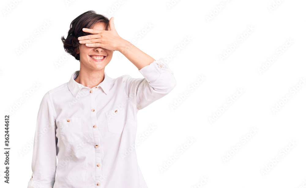Beautiful young woman with short hair wearing elegant white shirt smiling and laughing with hand on face covering eyes for surprise. blind concept. Beautiful young woman with short hair wearing elegant white shirt smiling and laughing with hand on face covering eyes for surprise. blind concept.