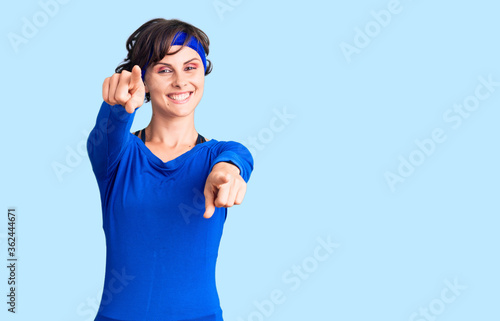 Beautiful young woman with short hair wearing training workout clothes pointing to you and the camera with fingers, smiling positive and cheerful