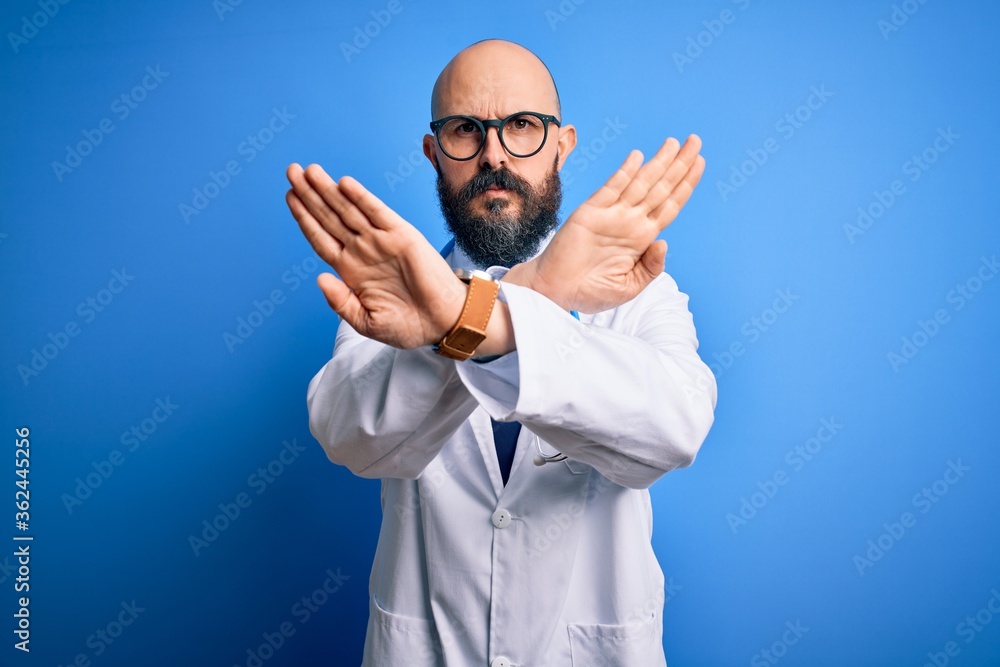 Handsome bald doctor man with beard wearing glasses and stethoscope over blue background Rejection expression crossing arms doing negative sign, angry face Handsome bald doctor man with beard wearing glasses and stethoscope over blue background Rejection expression crossing arms doing negative sign, angry face