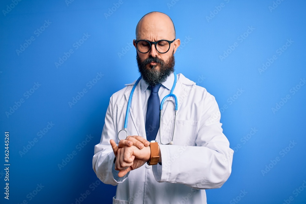 Handsome bald doctor man with beard wearing glasses and stethoscope over blue background Checking the time on wrist watch, relaxed and confident Handsome bald doctor man with beard wearing glasses and stethoscope over blue background Checking the time on wrist watch, relaxed and confident