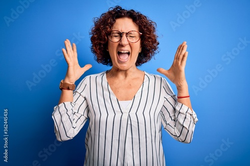 Middle age beautiful curly hair woman wearing casual striped shirt over isolated background celebrating mad and crazy for success with arms raised and closed eyes screaming excited. Winner concept
