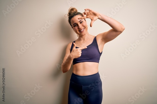 Young beautiful blonde sportswoman doing sport wearing sportswear over white background smiling making frame with hands and fingers with happy face. Creativity and photography concept.