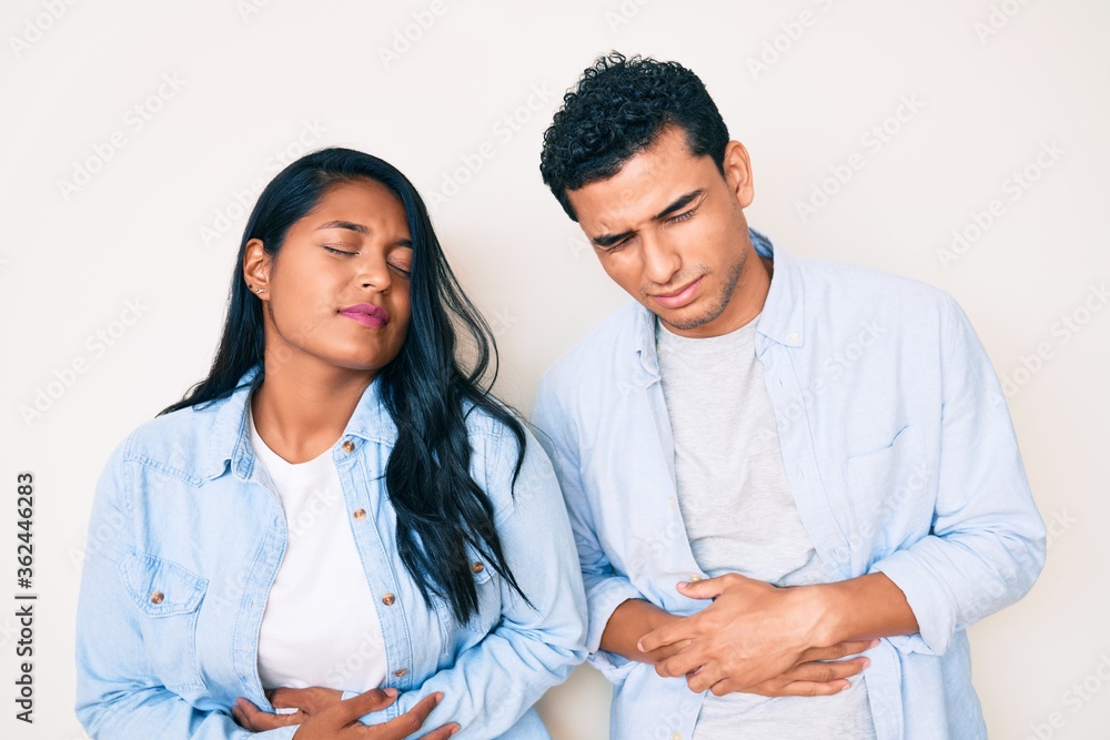 Beautiful latin young couple wearing casual clothes with hand on stomach because indigestion, painful illness feeling unwell. ache concept. Beautiful latin young couple wearing casual clothes with hand on stomach because indigestion, painful illness feeling unwell. ache concept.