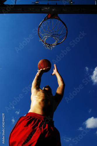 Bottom view of a man trying to shoot a ball into the hoop © ImageHit
