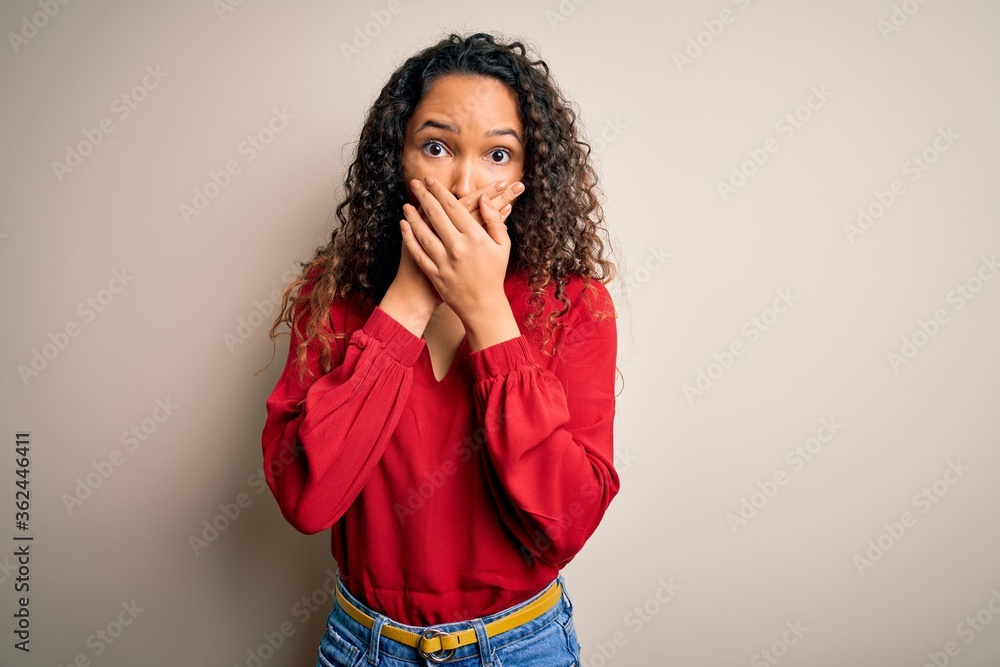 Young beautiful woman with curly hair wearing casual t-shirt standing over white background shocked covering mouth with hands for mistake. Secret concept. Young beautiful woman with curly hair wearing casual t-shirt standing over white background shocked covering mouth with hands for mistake. Secret concept.
