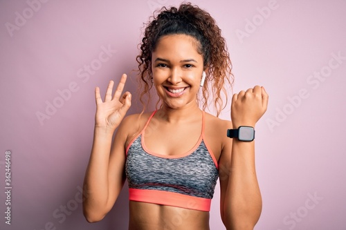 Beautiful sportswoman with curly hair doing sport wearing sportswear using smartwatch doing ok sign with fingers, excellent symbol © Krakenimages.com