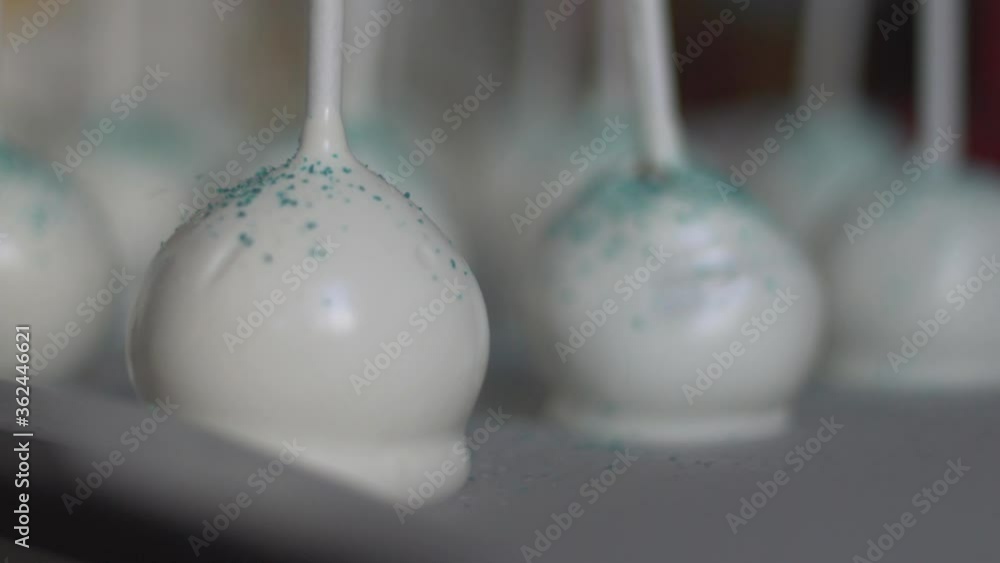 Close up of white cake pops, edible pastry glitter falling on them, slow motion 120fps Close up of white cake pops, edible pastry glitter falling on them, slow motion 120fps
