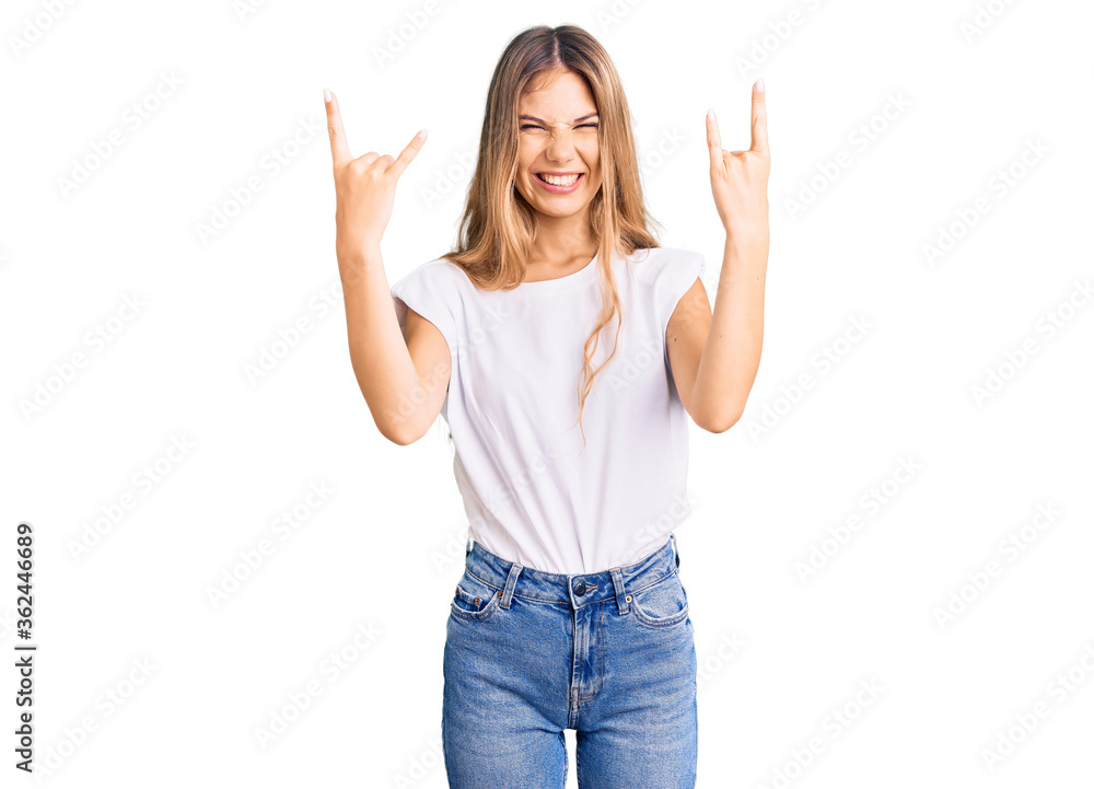 Beautiful caucasian woman with blonde hair wearing casual white tshirt shouting with crazy expression doing rock symbol with hands up. music star. heavy concept. Beautiful caucasian woman with blonde hair wearing casual white tshirt shouting with crazy expression doing rock symbol with hands up. music star. heavy concept.