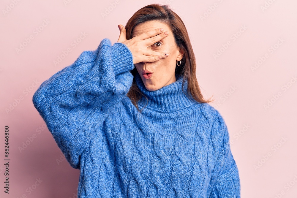 Young beautiful woman wearing winter sweater peeking in shock covering face and eyes with hand, looking through fingers afraid Young beautiful woman wearing winter sweater peeking in shock covering face and eyes with hand, looking through fingers afraid