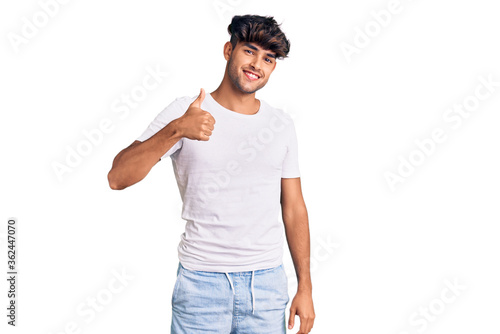Young hispanic man wearing casual clothes doing happy thumbs up gesture with hand. approving expression looking at the camera showing success.