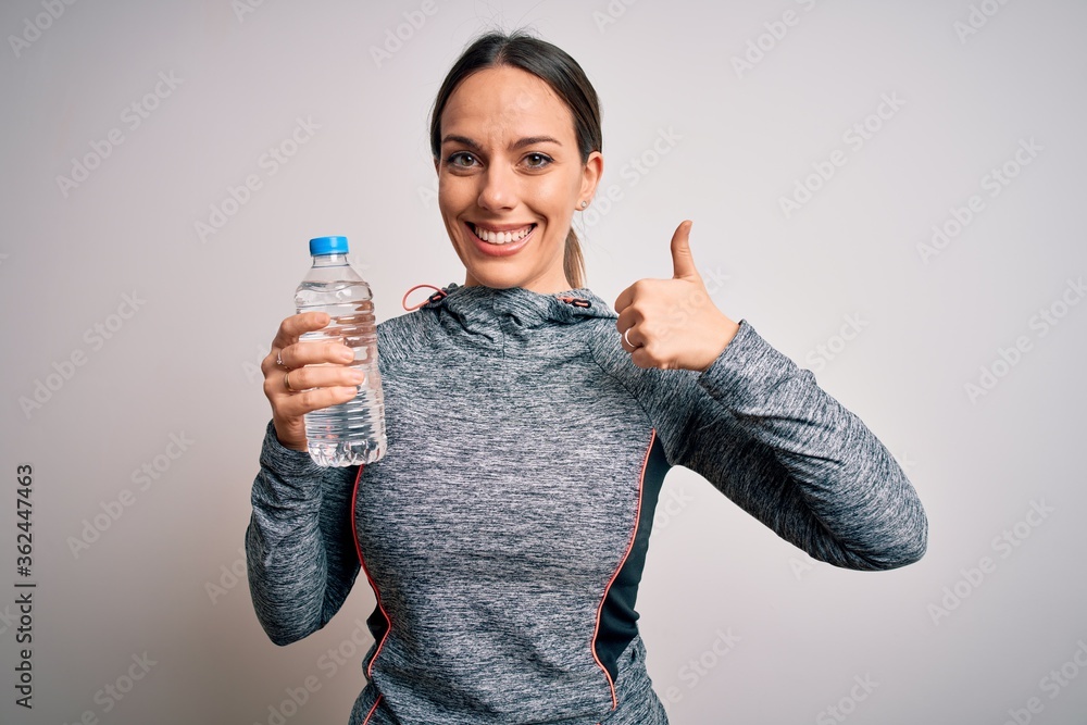 Young fitness woman wearing sport workout clothes drinking water from plastic bottle happy with big smile doing ok sign, thumb up with fingers, excellent sign Young fitness woman wearing sport workout clothes drinking water from plastic bottle happy with big smile doing ok sign, thumb up with fingers, excellent sign