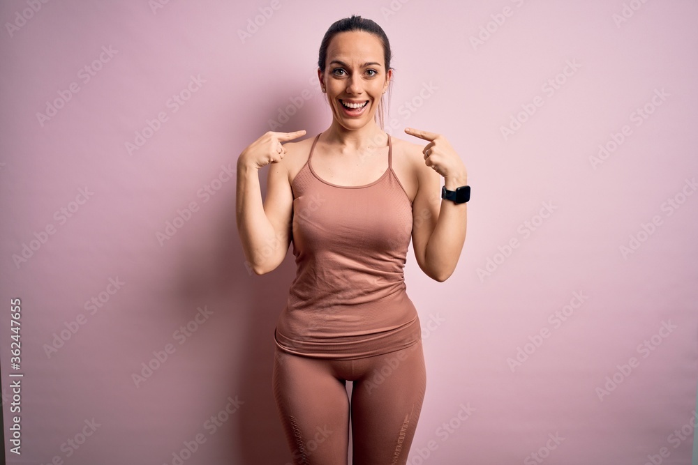 Young blonde fitness woman wearing sport workout clothes over pink isolated background looking confident with smile on face, pointing oneself with fingers proud and happy.