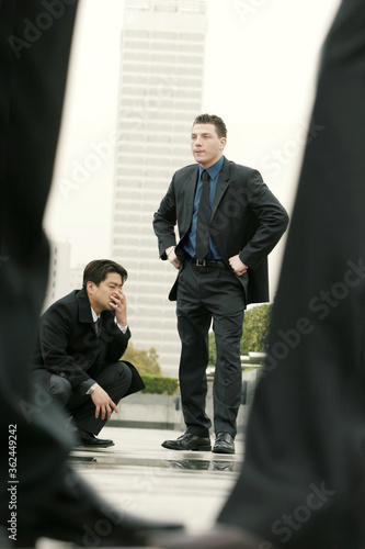 Tablou pe pânză An angry looking man and his Asian colleague waiting anxiously for their client