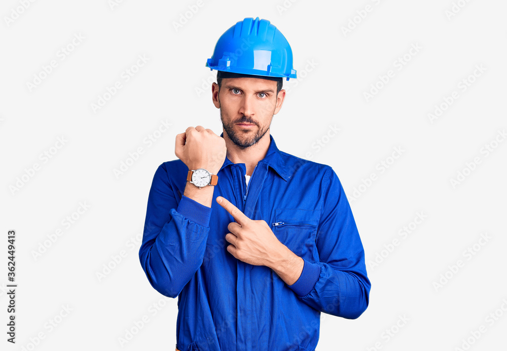 Young handsome man wearing worker uniform and hardhat checking the time on wrist watch, relaxed and confident Young handsome man wearing worker uniform and hardhat checking the time on wrist watch, relaxed and confident