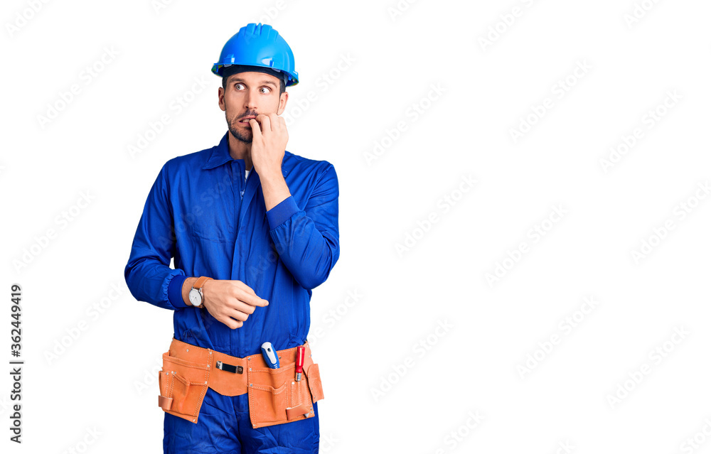 Young handsome man wearing worker uniform and hardhat pointing to both sides with fingers, different direction disagree