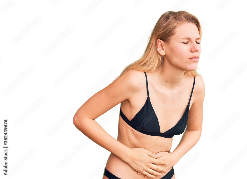 Young beautiful blonde woman wearing bikini with hand on stomach because indigestion, painful illness feeling unwell. ache concept. Young beautiful blonde woman wearing bikini with hand on stomach because indigestion, painful illness feeling unwell. ache concept.
