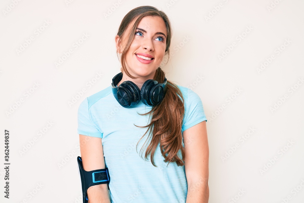 Beautiful young caucasian woman wearing gym clothes and using headphones looking away to side with smile on face, natural expression. laughing confident. Beautiful young caucasian woman wearing gym clothes and using headphones looking away to side with smile on face, natural expression. laughing confident.