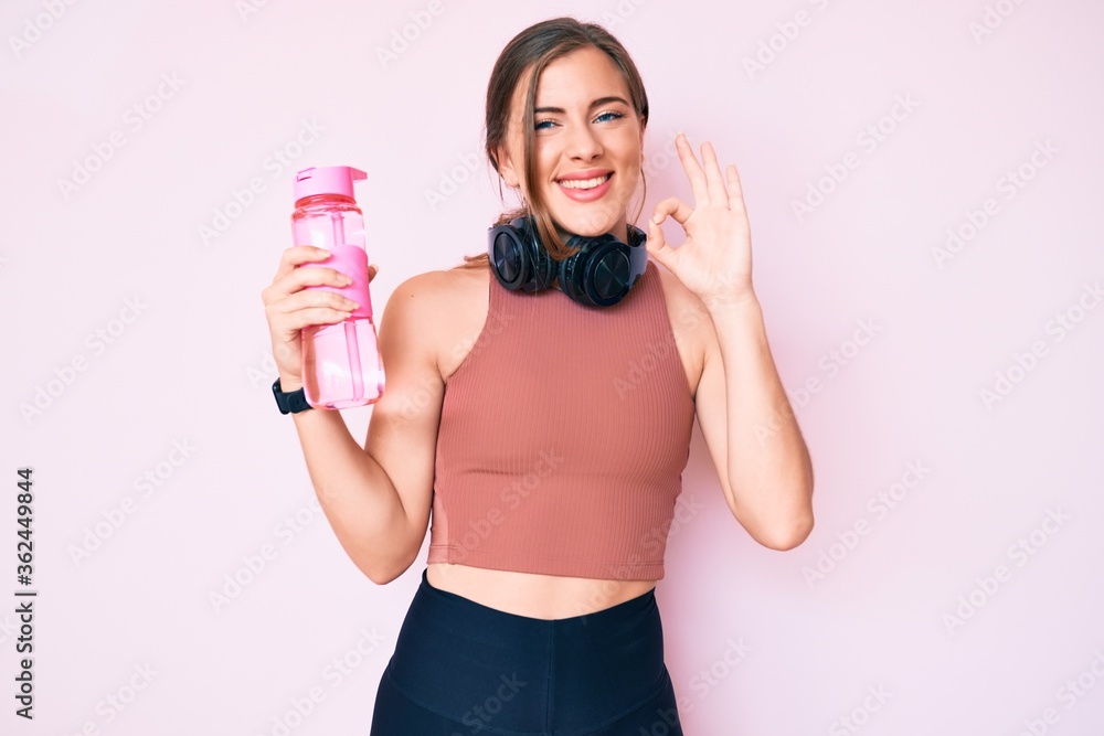 Beautiful young caucasian woman wearing sportswear holding water bottle doing ok sign with fingers, smiling friendly gesturing excellent symbol Beautiful young caucasian woman wearing sportswear holding water bottle doing ok sign with fingers, smiling friendly gesturing excellent symbol