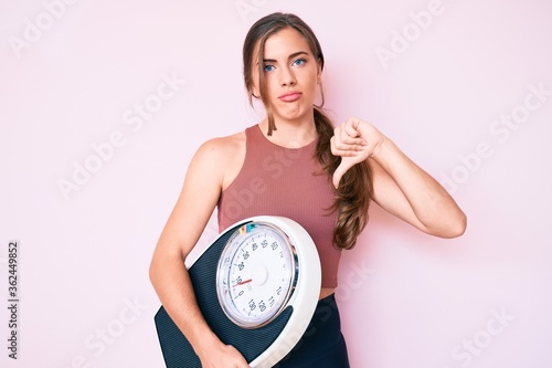 Konstfotografi Beautiful young caucasian woman holding weight machine to balance weight loss wi