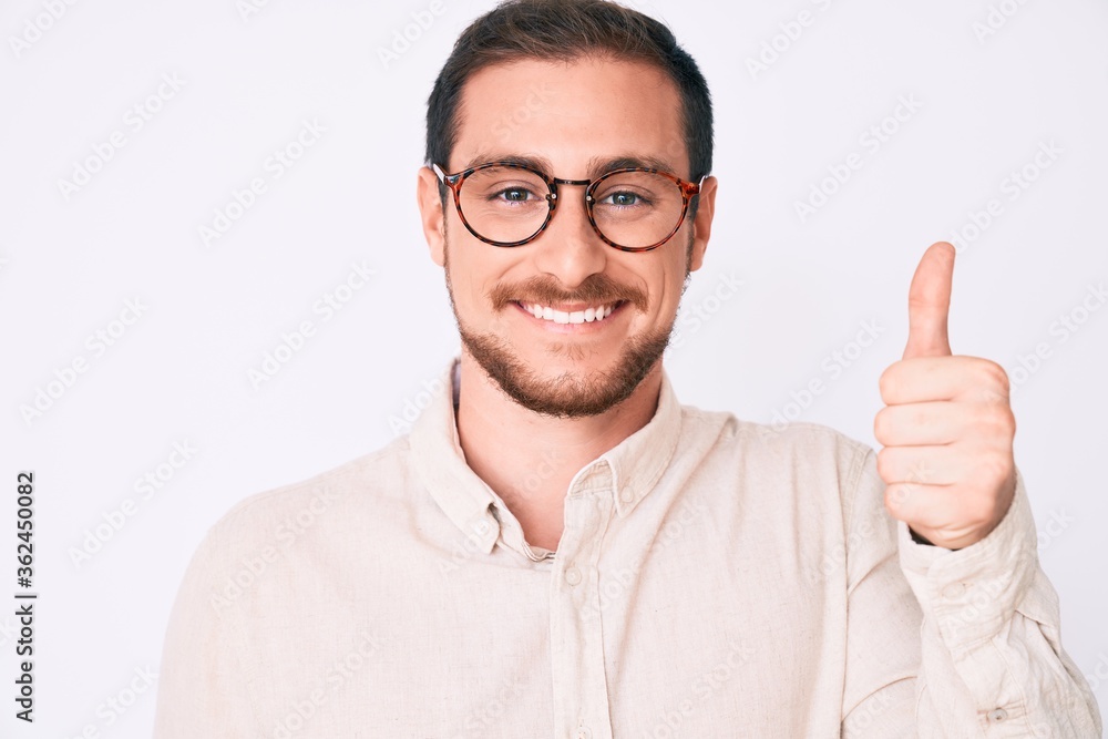 Fototapeta premium Young handsome man wearing casual clothes and glasses smiling happy and positive, thumb up doing excellent and approval sign