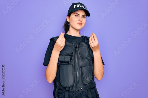 Young police woman wearing security bulletproof vest uniform over purple background doing money gesture with hands, asking for salary payment, millionaire business