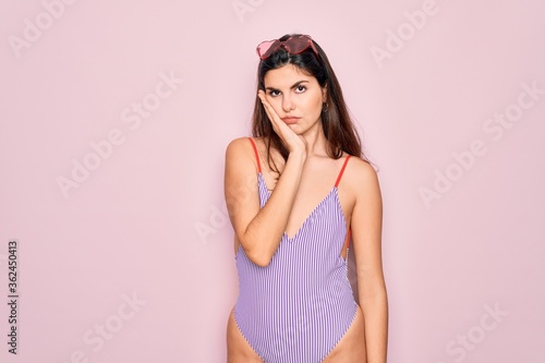Young beautiful fashion girl wearing swimwear swimsuit and sunglasses over pink background thinking looking tired and bored with depression problems with crossed arms.
