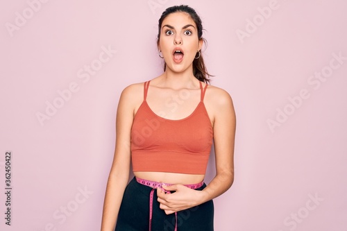 Young beautiful fitness woman wearing sport excersie clothes using measuring tape scared in shock with a surprise face, afraid and excited with fear expression © Krakenimages.com