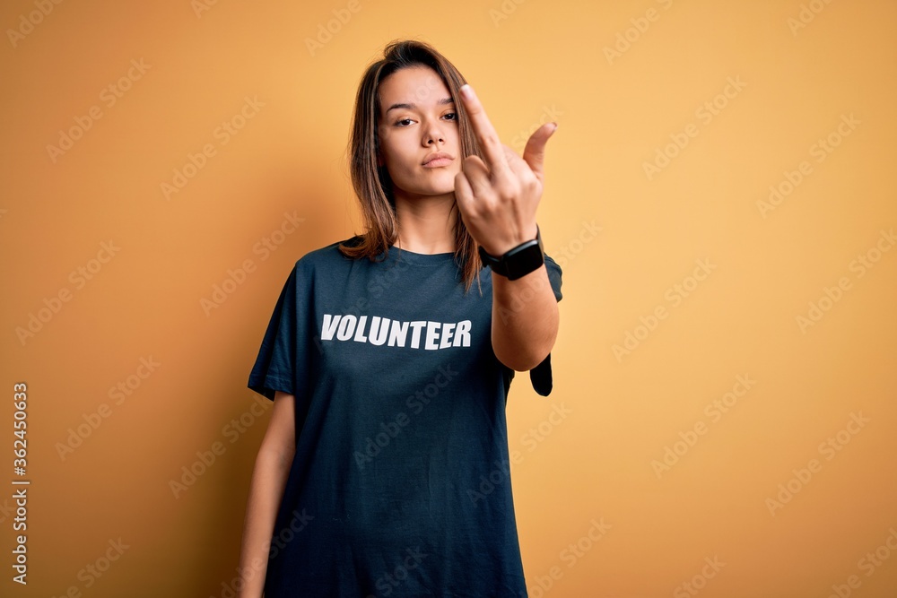 Young beautiful brunette girl doing volunteering wearing t-shirt with volunteer message word Showing middle finger, impolite and rude fuck off expression Young beautiful brunette girl doing volunteering wearing t-shirt with volunteer message word Showing middle finger, impolite and rude fuck off expression
