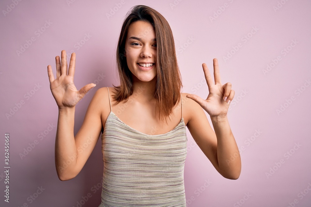 Young beautiful brunette girl wearing casual striped t-shirt over isolated pink background showing and pointing up with fingers number eight while smiling confident and happy. Young beautiful brunette girl wearing casual striped t-shirt over isolated pink background showing and pointing up with fingers number eight while smiling confident and happy.