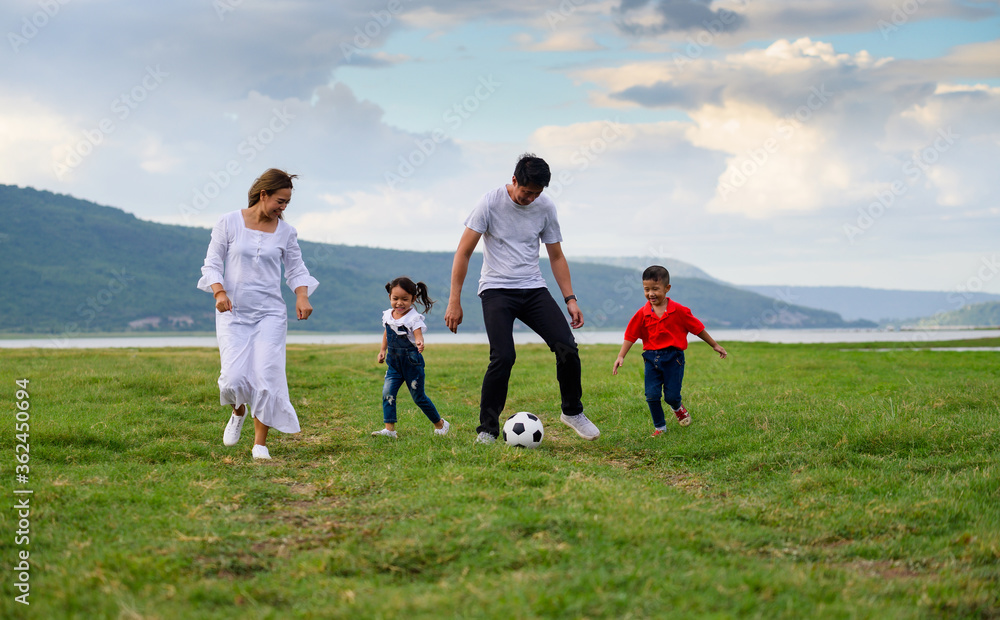 Cheerful family Asian playing football in a green lawn Cheerful family Asian playing football in a green lawn