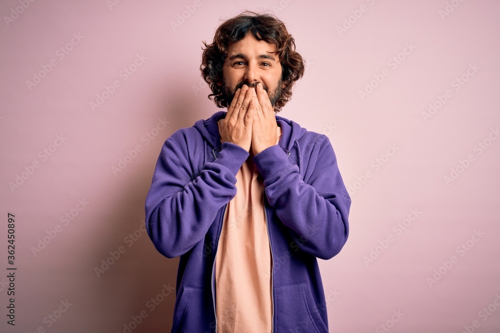 Young handsome sporty man with beard wearing casual sweatshirt over pink background laughing and embarrassed giggle covering mouth with hands, gossip and scandal concept Young handsome sporty man with beard wearing casual sweatshirt over pink background laughing and embarrassed giggle covering mouth with hands, gossip and scandal concept