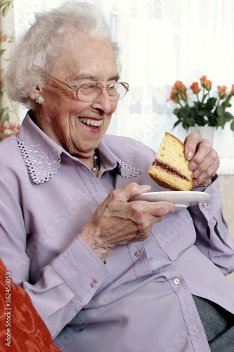 фотографія An old bespectacled woman sitting on the couch eating cake