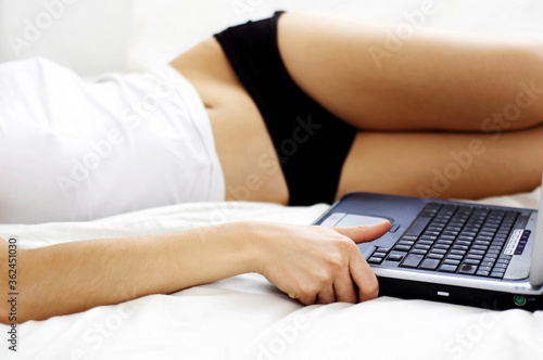 Chest down shot of a woman lying on the bed with a laptop by her side