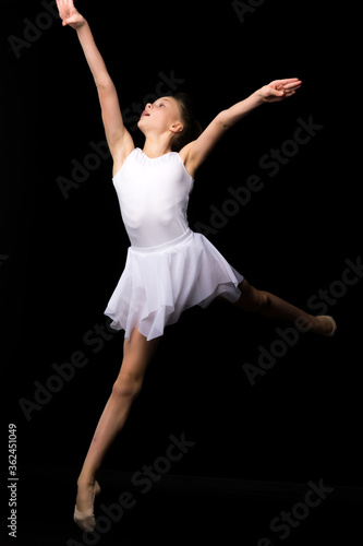 Girl gymnast in the studio on a black background performs gymnastic exercises
