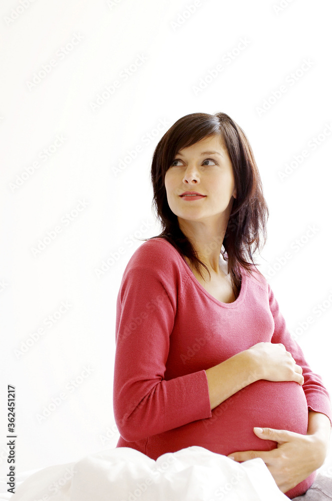 A pregnant lady sitting on the bed touching her stomach A pregnant lady sitting on the bed touching her stomach