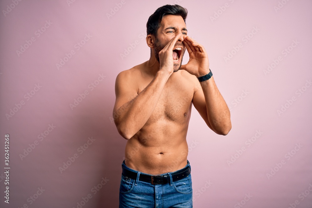 Fototapeta premium Young handsome strong man with beard shirtless standing over isolated pink background Shouting angry out loud with hands over mouth