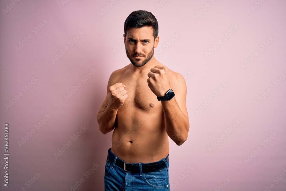 Young handsome strong man with beard shirtless standing over isolated pink background Ready to fight with fist defense gesture, angry and upset face, afraid of problem