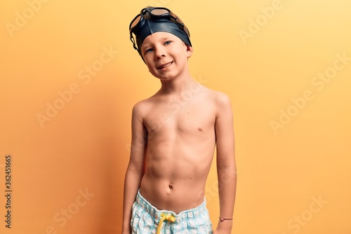 Cute blond kid wearing swimwear and swimmer glasses looking positive and happy standing and smiling with a confident smile showing teeth © Krakenimages.com
